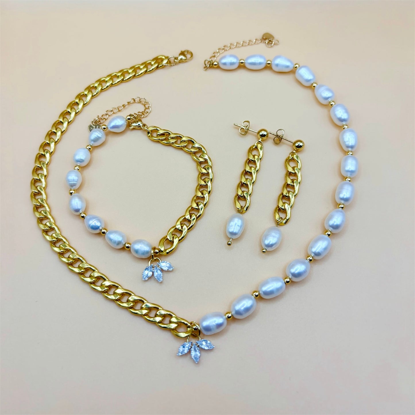 Gold jewelry set with pearl and chain necklace, bracelet, and earrings on a beige background