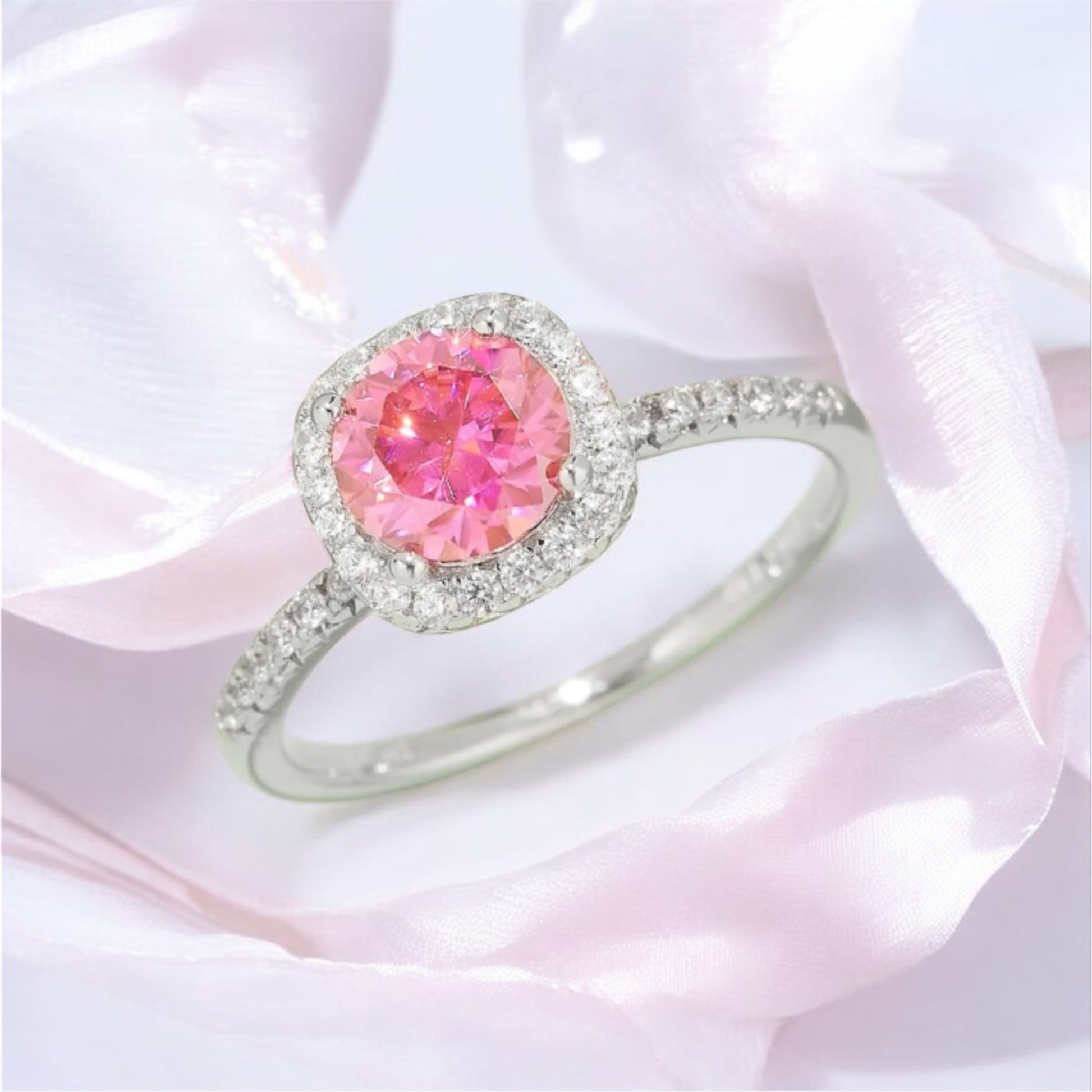 1 carat pink Moissanite halo ring with a silver band accented with moissanite stones on a pink fabric  