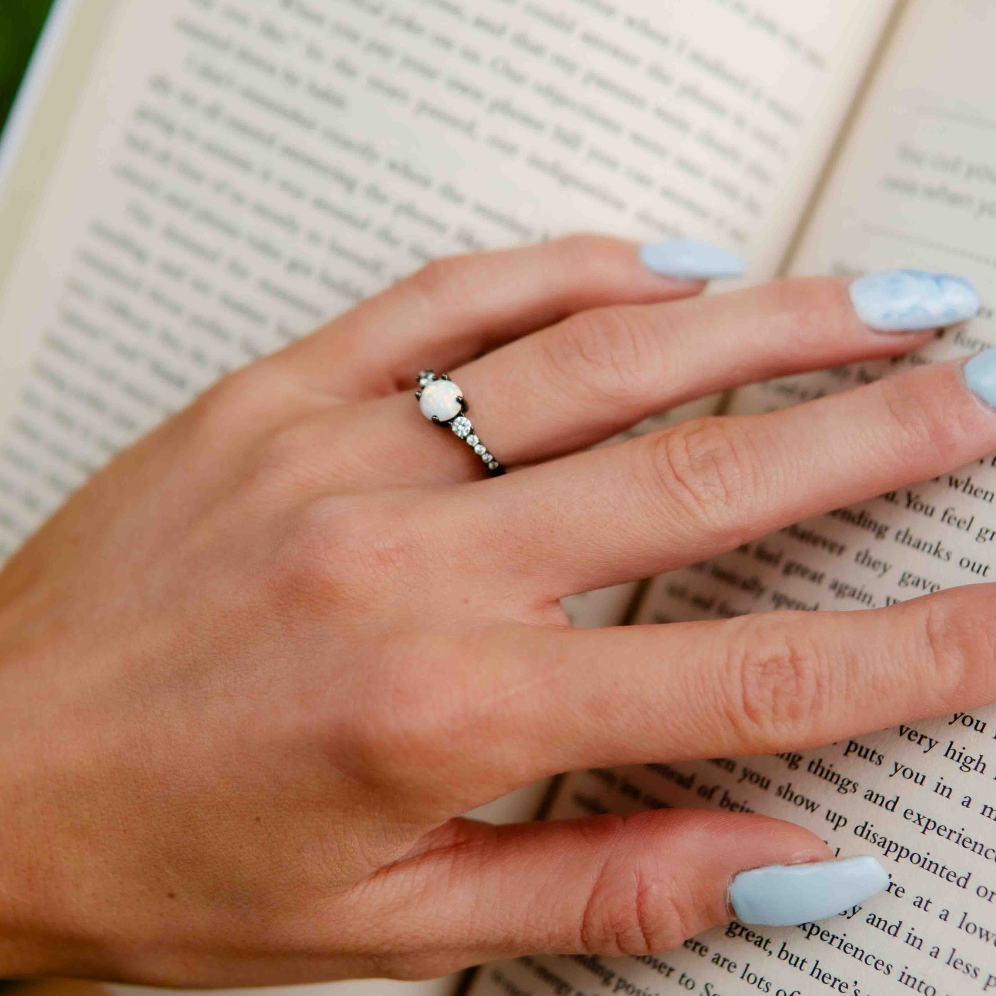 Opal gold-plated ring ,Kim, on girl holding her hand on a book