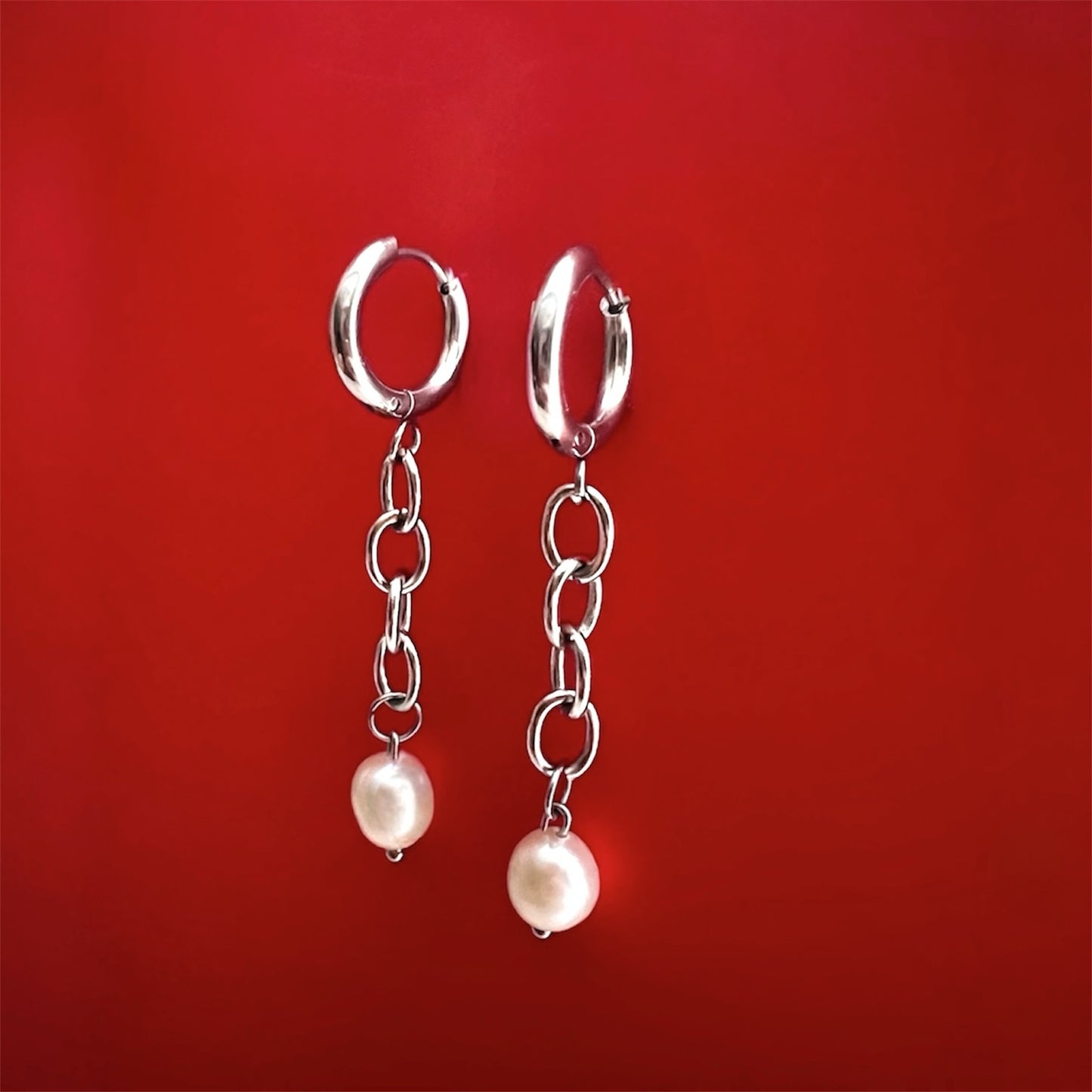 Unchained Monique silver chain earrings, side angle showing length and design, red background