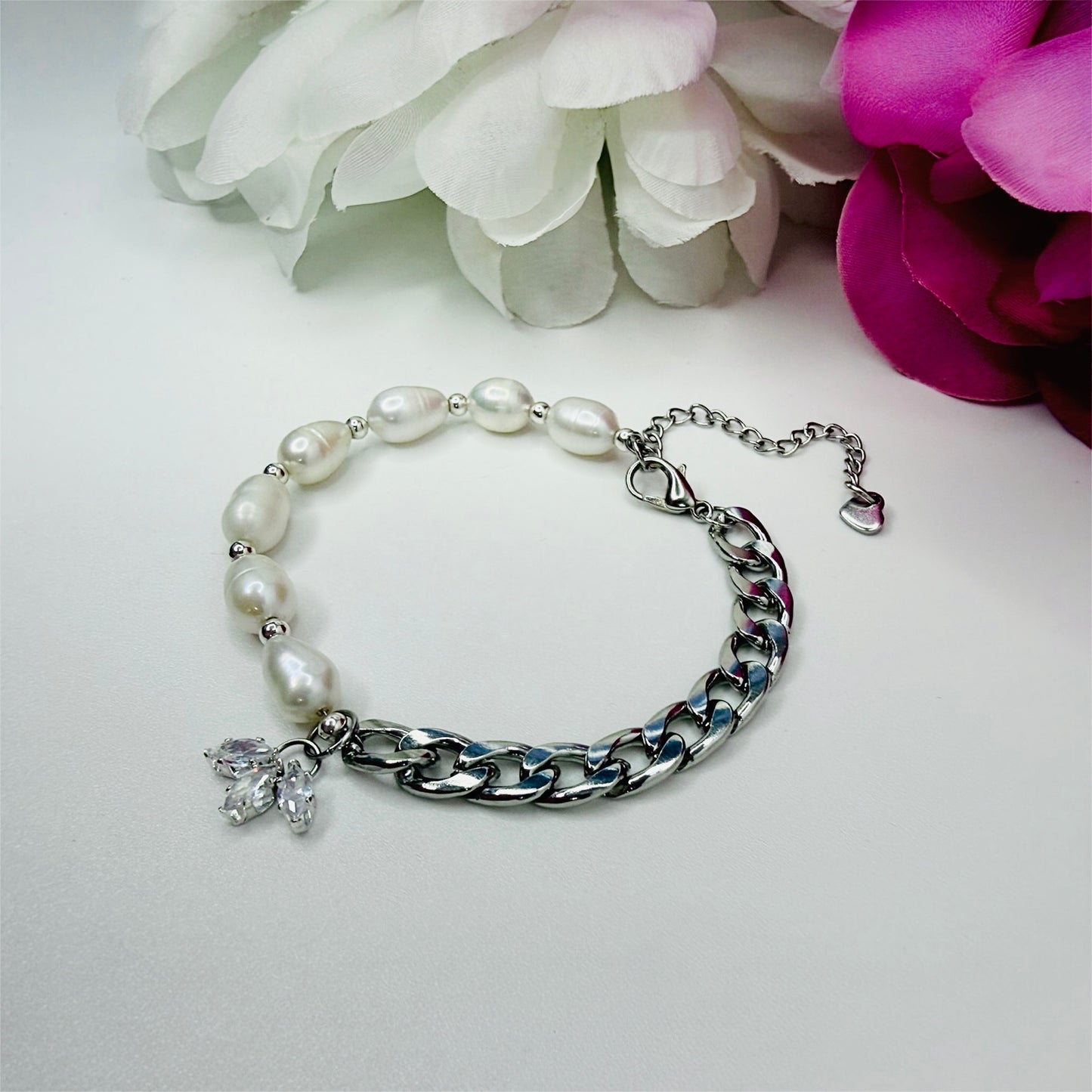 Cuban chain and freshwater pearl bracelet, with a flower looking charm, on a white background with pink and white flowers 