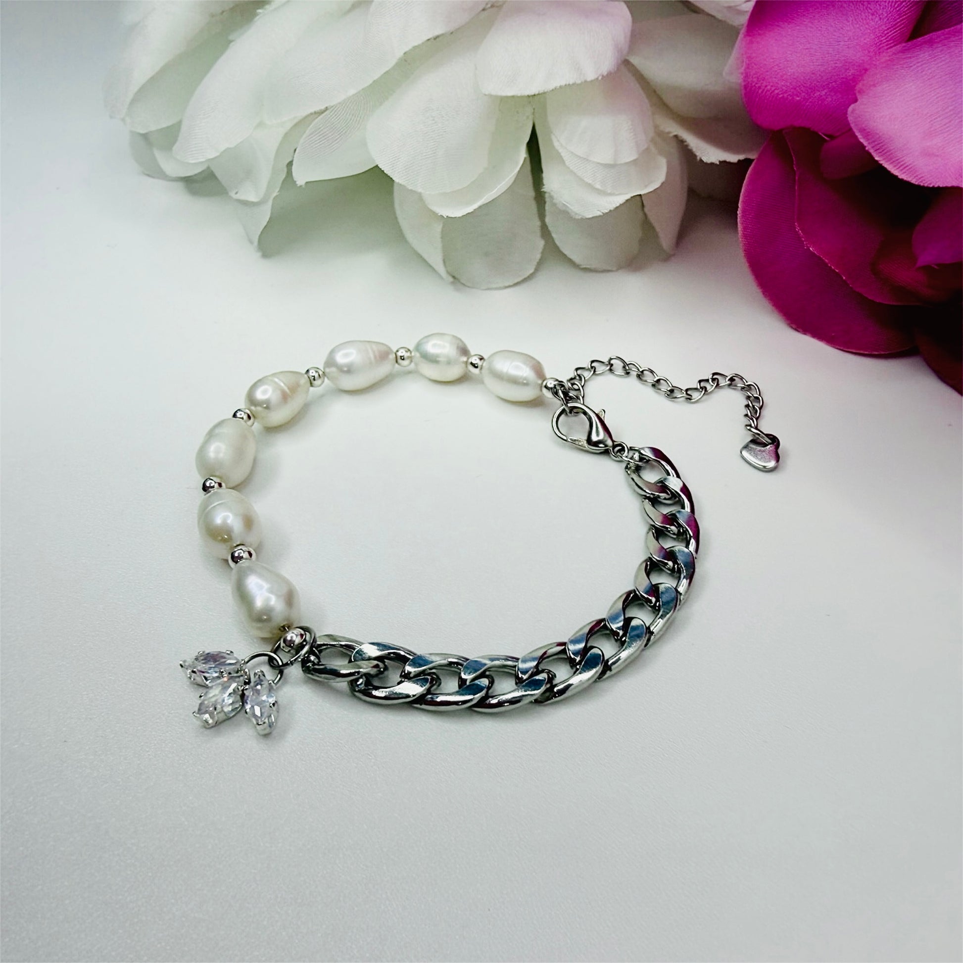 Cuban chain and freshwater pearl bracelet, with a flower looking charm, on a white background with pink and white flowers 