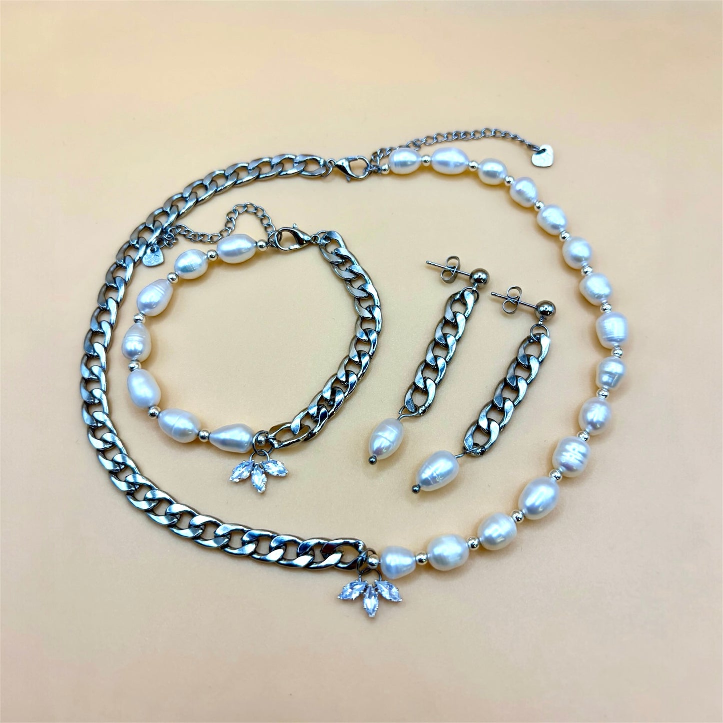 Silver jewelry set with pearl and chain necklace, bracelet, and earrings on a beige background