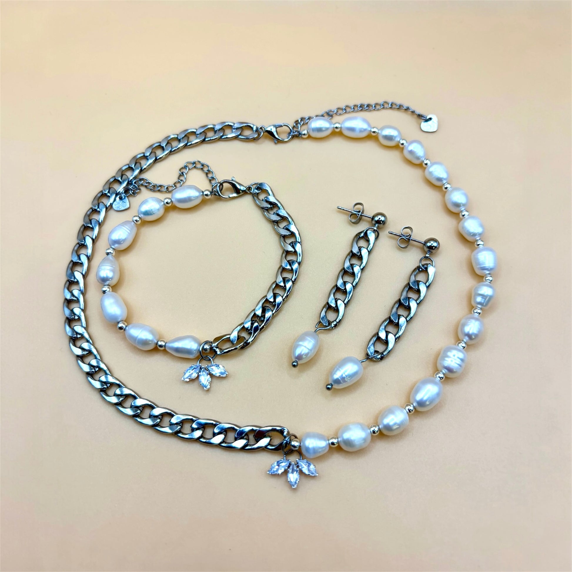 Silver jewelry set with pearl and chain necklace, bracelet, and earrings on a beige background