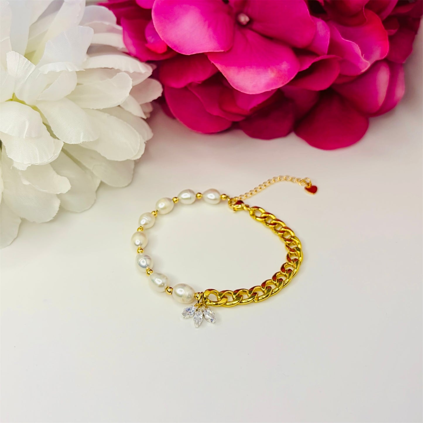 Gold cuban chain bracelet with natural freshwater pearls on a white background with pink flowers