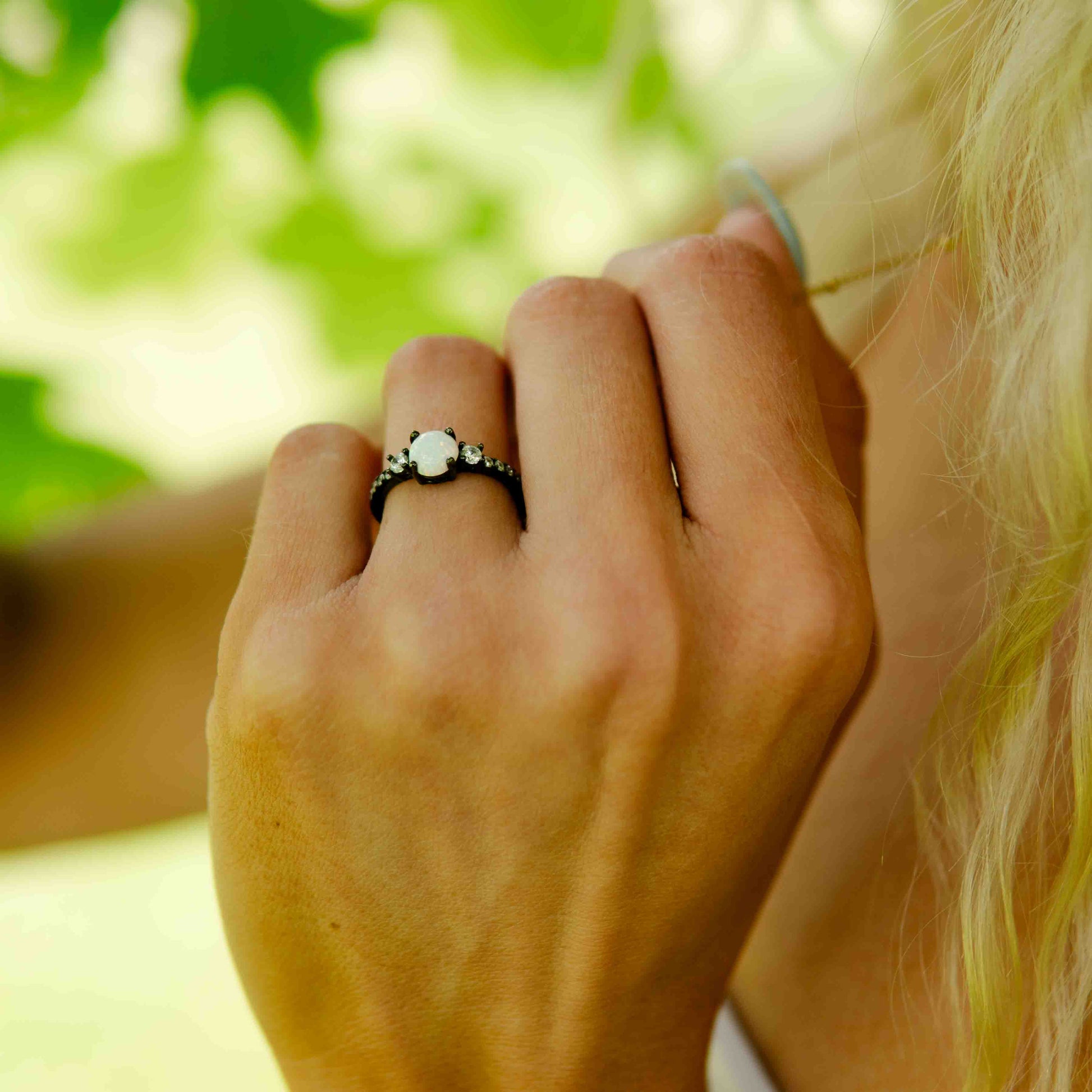 Close-up of a hand wearing an opal black ring with a blurred green background