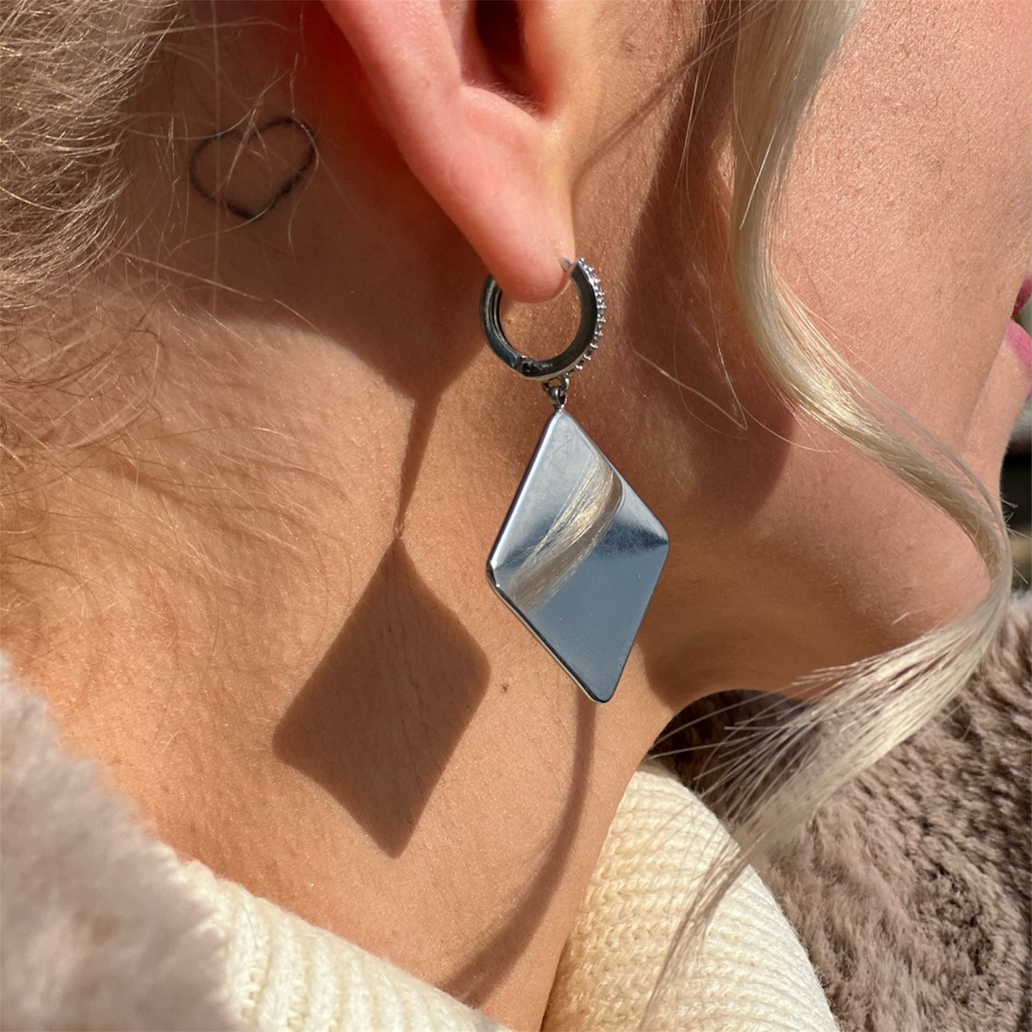 Close-up of a silver geometric earring worn by a person with blonde hair.
